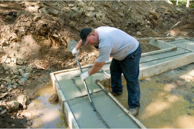 Worker leveling concrete foundation with a shovel